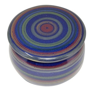 Könnte beinhalten: Eine blaue und grüne Keramik-Butterdose mit Deckel. Der Deckel hat ein konzentrisches Kreis-Muster in Blautönen, Grüntönen und Rot.