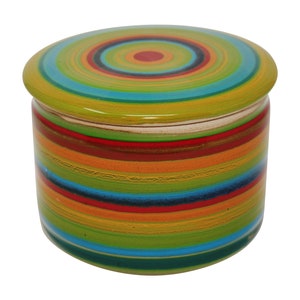 Könnte beinhalten: Eine farbenfrohe Butterdose aus Keramik mit einem gestreiften Design in Grün-, Blau-, Rot-, Orange- und Gelbtönen. Der Deckel hat ein konzentrisches Kreisdesign.