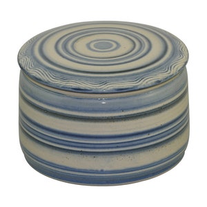 Könnte beinhalten: Eine weiße Keramik-Butterdose mit blau-weißem Streifenmuster. Der Deckel hat ein konzentrisches Kreisdesign.