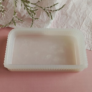 May include: A rectangular, semi-translucent white tray with a ribbed, scalloped edge design. The tray features a smooth, flat interior surface and a consistent, milky off-white color throughout its structure, presenting a clean and simple form.