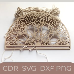 May include: A wooden cutout of a mandala design in the shape of a half circle. The mandala is intricate and detailed, with a floral pattern. The cutout is on a white background and has white string attached to it.