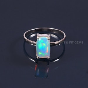 Puede incluir: Un anillo de plata con una piedra de ópalo rectangular. El ópalo es iridiscente con tonos de azul, verde y naranja.