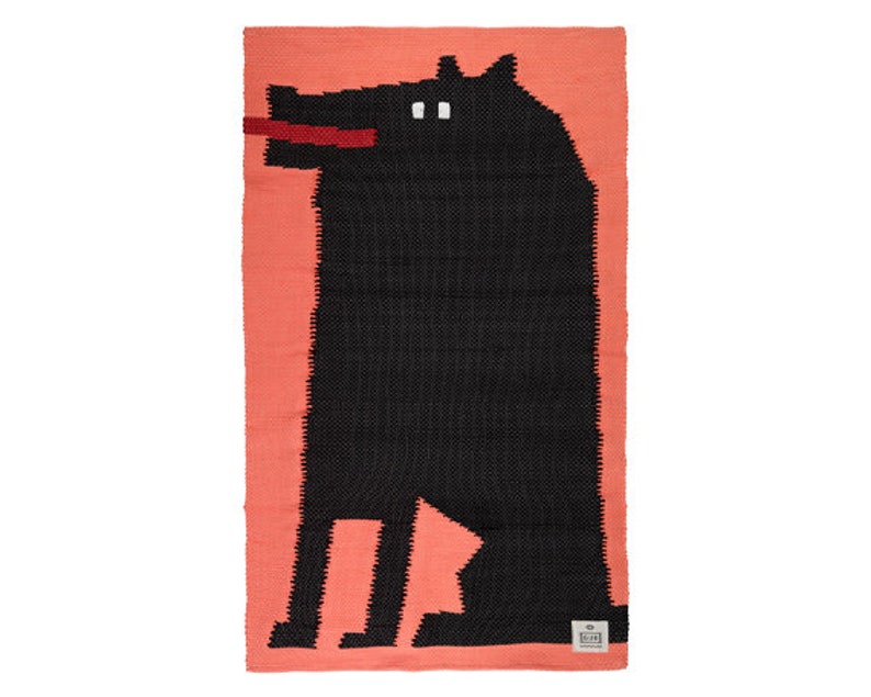 May include: A black and white woven rug with a silhouette of a dog sitting on a coral pink background.