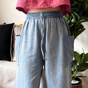 May include: A cropped, long-sleeved, V-neck top in a vibrant pink hue paired with light blue, wide-leg pants. The pants feature large pockets and a drawstring waist. The outfit is casual and comfortable, suitable for everyday wear.