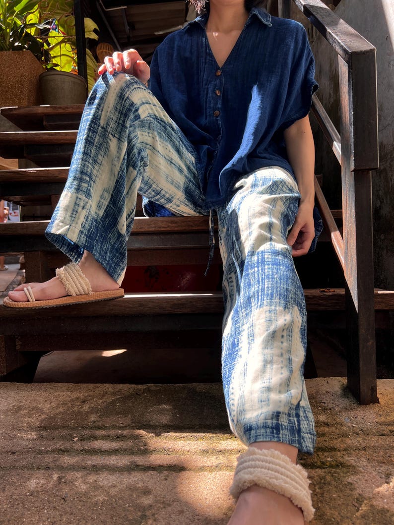 Model wearing indigo wide-leg cotton pants with elastic drawstring waist with an indigo relaxed fit buttoned up shirt sitting on stairs