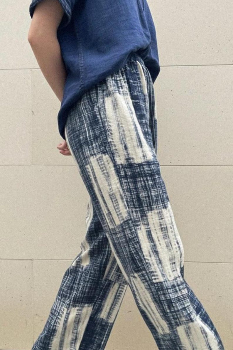 May include: Loose-fitting, navy blue and white patterned pants. The pants have a wide-leg design with a repeating pattern of vertical and horizontal lines. The model is also wearing a navy blue top.