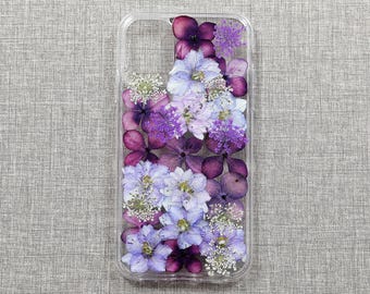 May include: A clear phone case with a pressed flower design. The flowers are purple and light blue.