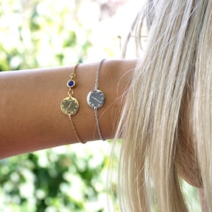 Könnte beinhalten: Zwei zarte Armbänder mit einem runden Uhrendesign. Ein Armband ist golden mit einem blauen Edelstein-Akzent, das andere ist silber.