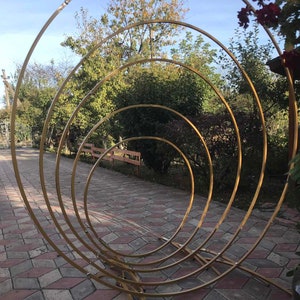 May include: A gold metal archway made of four concentric circles. The archway is standing on a brick patio.