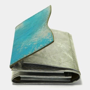 May include: A folded leather wallet with a turquoise blue flap and a silver metallic body.