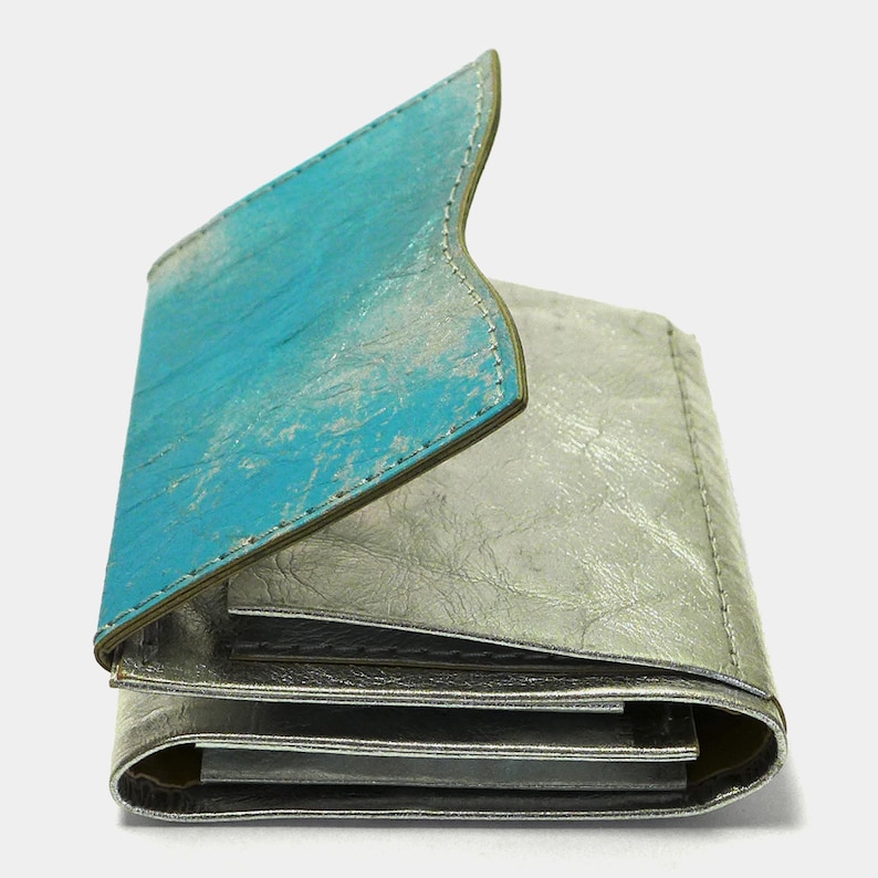 May include: A folded leather wallet with a turquoise blue flap and a silver metallic body.
