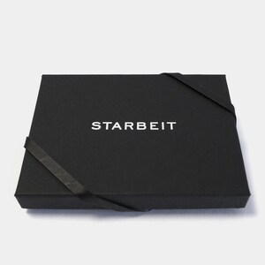 May include: A black box with a white ribbon and the word "STARBEIT" printed on the top.
