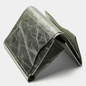 May include: A silver leather wallet with a folded design. The wallet is made of a soft, textured leather and has a subtle sheen.