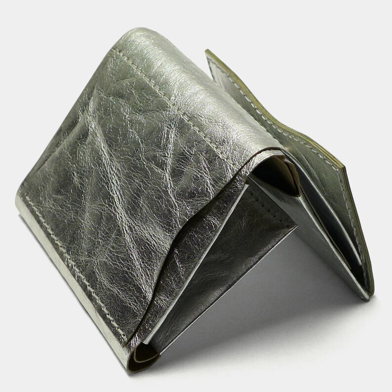 May include: A silver leather wallet with a folded design. The wallet is made of a soft, textured leather and has a subtle sheen.