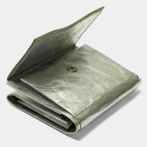 May include: A silver leather wallet with a fold-over closure and a snap button. The wallet is folded closed and the inside is visible.