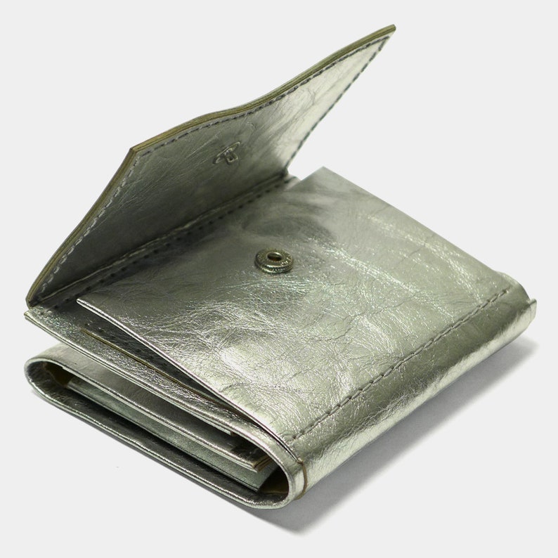 May include: A silver leather wallet with a fold-over closure and a snap button. The wallet is folded closed and the inside is visible.