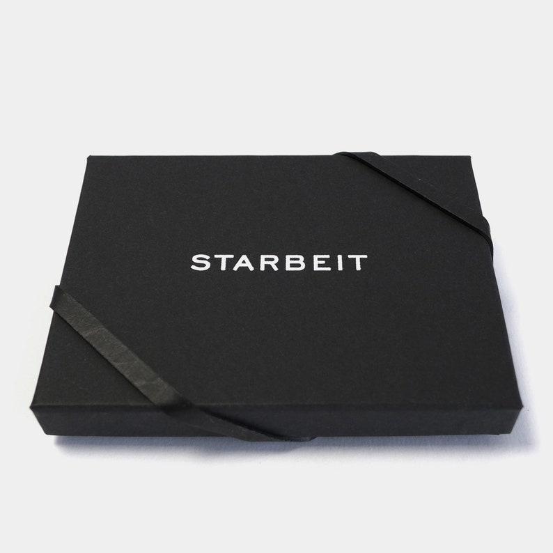 May include: A black box with a white ribbon and the word "STARBEIT" printed on the top.