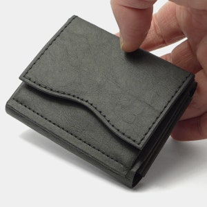 May include: A black leather wallet with a fold-over flap and a stitched design. The wallet is folded closed and held in a hand.