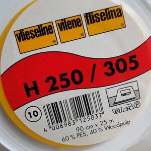 Può includere: Un rotolo bianco di interfodera termoadesiva con un'etichetta gialla e rossa. L'etichetta dice "vlieseline vilene fliselina" e "H 250/305". L'etichetta include anche un codice a barre, un numero 10 e istruzioni per la stiratura.
