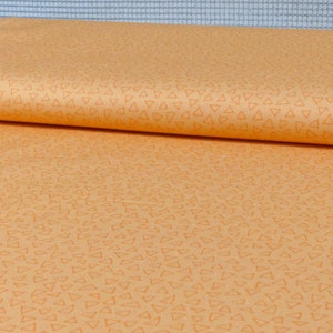 Könnte beinhalten: Ein Stoff mit hellorangefarbenem Hintergrund und einem Muster aus kleinen, weißen Dreiecken.