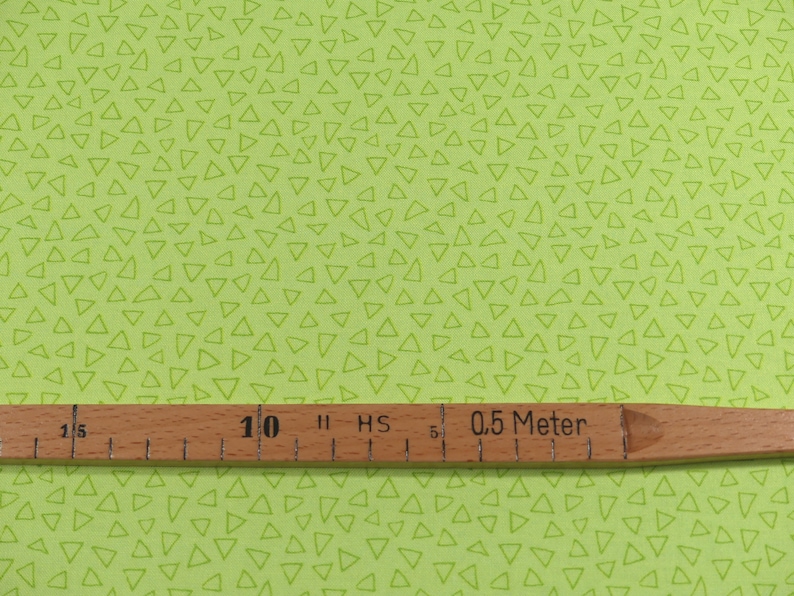 以下が含まれることがあります： 白い三角形の模様がついた緑色の布。布の上に「0.5メートル」と書かれた木製の定規が置かれている。