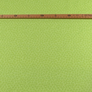 以下が含まれることがあります： 小さな手書きの三角形が繰り返しパターンになっている緑色の生地。生地の上に、インチとセンチの目盛りがついた木製の定規が置かれている。