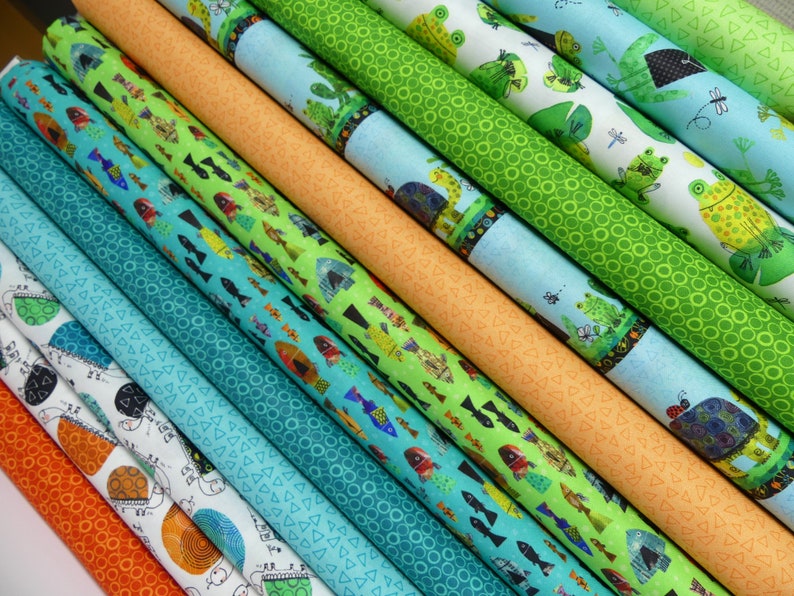 以下が含まれることがあります： 魚、カエル、幾何学模様など、さまざまなパターンが施されたカラフルな生地のロールの集まりです。生地はロール状に巻かれ、一列に並べてあり、鮮やかな色とユニークなプリントが際立っています。