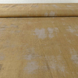 May include: A close-up of a fabric with a textured, distressed look. The fabric is a light brown color with a subtle pattern of white and gray.