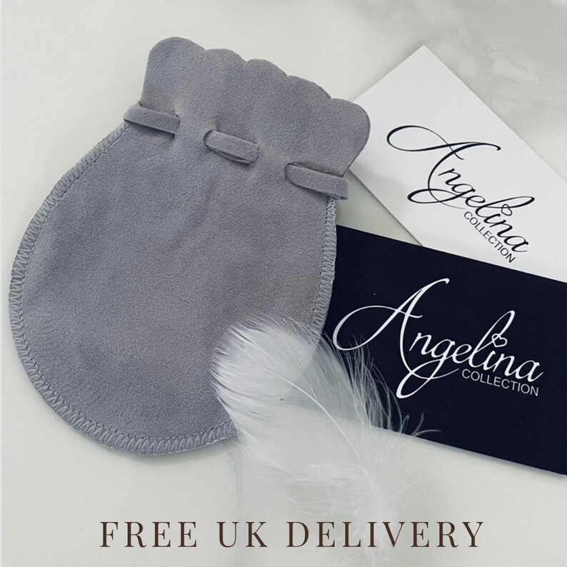 May include: A grey suede-like drawstring pouch with a scalloped top edge, accompanied by a white feather and two rectangular cards featuring the text Angelina Collection in a script font, one white and one dark blue.