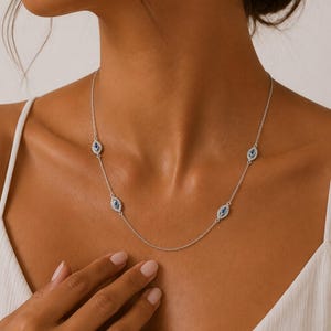 May include: A silver-toned chain necklace featuring four evenly spaced eye-shaped charms. Each charm is outlined with small clear stones and contains a central dark blue stone, creating a delicate and symmetrical design around the neckline.