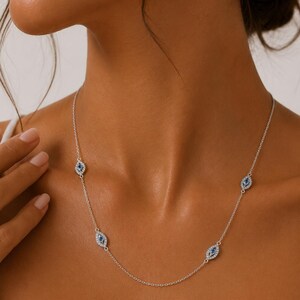 May include: A silver-toned chain necklace featuring four evenly spaced eye-shaped charms. Each charm is outlined with small clear stones and contains a central dark blue stone, creating a repeating pattern along the delicate metal link chain.