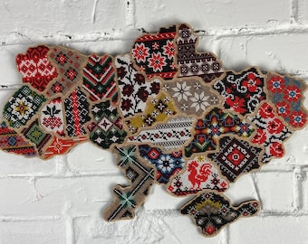 May include: A colorful embroidered map of Ukraine, made of fabric patches with traditional Ukrainian patterns. The map is shaped like the country's outline and features a variety of colors and designs.