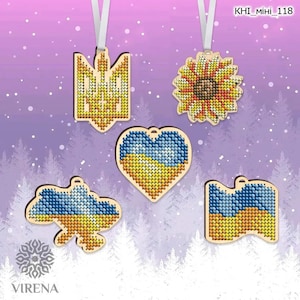 May include: Wooden ornaments with Ukrainian flag and sunflower designs. Each ornament is adorned with a stitched pattern in blue, yellow, and brown hues. They hang from white ribbons against a wintery background.