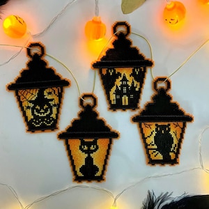 May include: Four black and orange Halloween lantern decorations with different designs, including a witch, haunted house, black cat, and owl. The lanterns are strung with gold thread and lit with small orange lights.