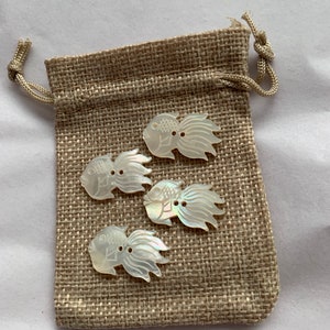 May include: Four white mother of pearl buttons shaped like fish with detailed carvings. The buttons are in a small burlap bag with a drawstring.