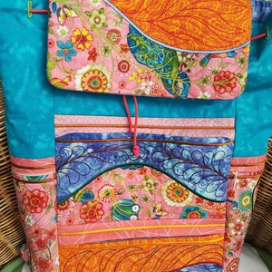 Könnte beinhalten: Eine farbenfrohe, gesteppte Tragetasche mit Klappenverschluss. Die Tasche weist eine lebendige Mischung aus Blumen- und Paisley-Mustern in Pink, Orange, Blau und Türkis auf. Das Design umfasst gestickte Details und einen Kordelzugverschluss, der einen einzigartigen, handgefertigten Stil zeigt.