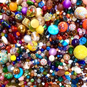 Könnte beinhalten: Eine große Sammlung verschiedener Bastelperlen in unterschiedlichen Formen, Größen und Farben, darunter Materialien aus Glas, Kunststoff und Metall. Die Mischung umfasst florale Muster, solide opake und durchscheinende Oberflächen, goldene Akzente und Texturen.