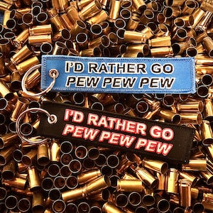 May include: Two keychains with the text "I'd rather go pew pew pew" in white on a blue background and red on a black background. The keychains are surrounded by gold bullet casings.