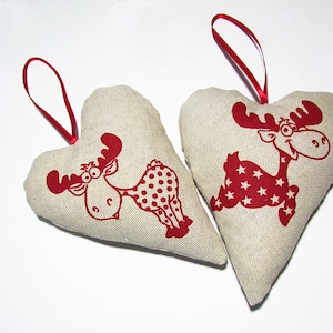 Könnte beinhalten: Zwei beigefarbene herzförmige Ornamente mit roten Rentier-Designs. Ein Rentier hat rote Punkte und das andere rote Sterne.