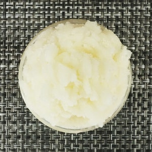 May include: A close-up of a white, grainy substance in a clear glass bowl. The substance appears to be a sugar scrub or a similar product.