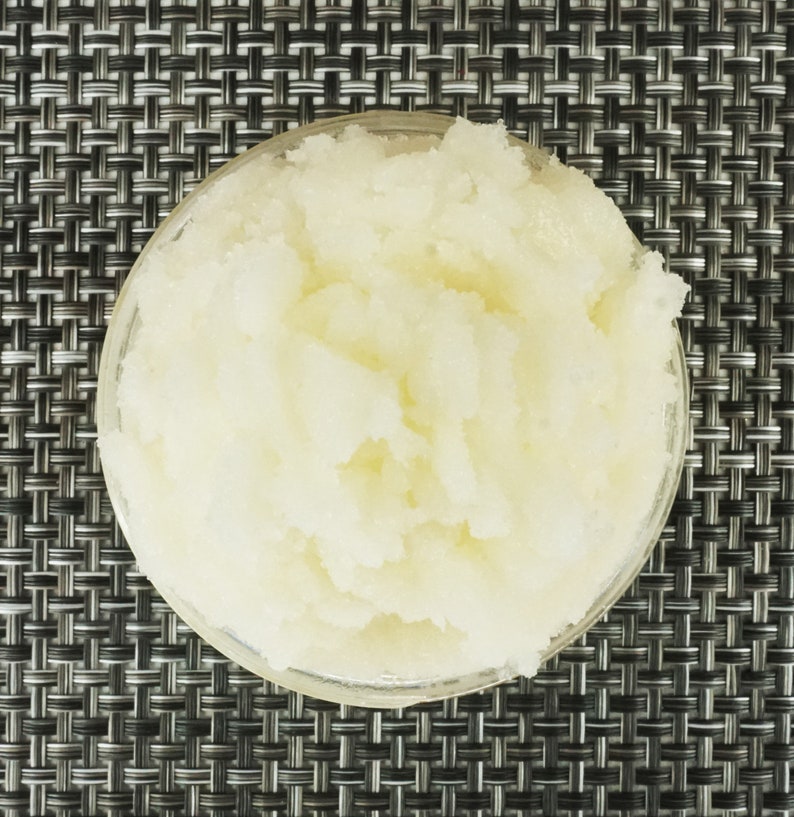 May include: A close-up of a white, grainy substance in a clear glass bowl. The substance appears to be a sugar scrub or a similar product.