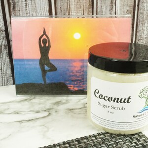 May include: A clear glass jar with a black lid filled with a white sugar scrub. The label reads "Coconut Sugar Scrub 8 oz Natural Gifts".