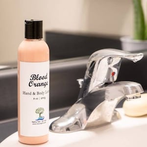 May include: A clear bottle with a black lid and a pink lotion inside. The bottle has a white label with the text "Blood Orange Hand & Body Lotion 8 oz | 236g Natural Oils www.naturaloils.com".
