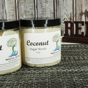 May include: Two glass jars of coconut sugar scrub, each with a white label that reads "Coconut Sugar Scrub 8 oz" and "Natural Gift". The jars are sitting on a brown and white woven placemat. A wooden sign that reads "Relax" is in the background.