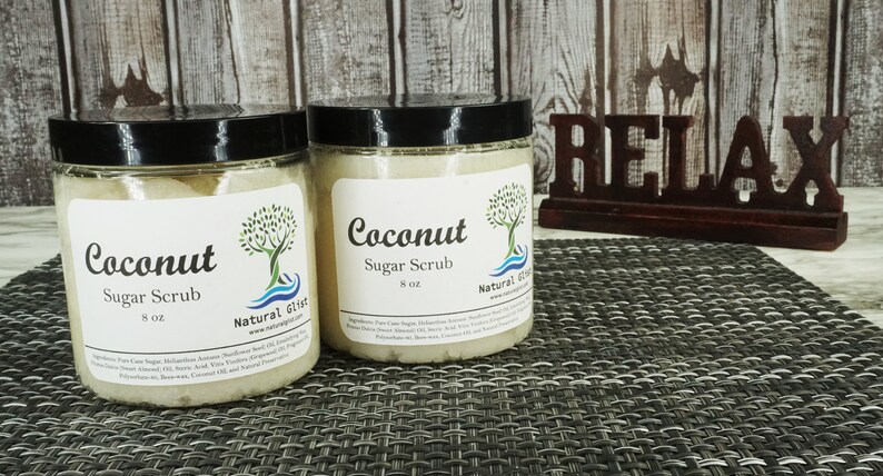 May include: Two glass jars of coconut sugar scrub, each with a white label that reads "Coconut Sugar Scrub 8 oz" and "Natural Gift". The jars are sitting on a brown and white woven placemat. A wooden sign that reads "Relax" is in the background.