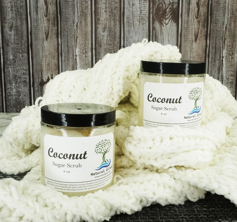 May include: Two glass jars of coconut sugar scrub, each with a black lid and a white label that says "Coconut Sugar Scrub" and "Natural  Slist". The jars are sitting on a white knitted blanket.