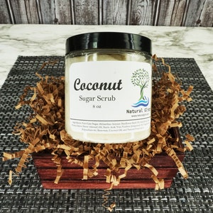 May include: A glass jar with a black lid filled with a white sugar scrub. The label reads "Coconut Sugar Scrub 8 oz" and "Natural Glist".