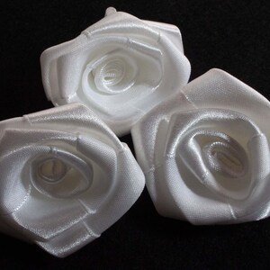 Könnte beinhalten: Drei weiße Satinbandrosen. Die Rosen sind in einer Gruppe angeordnet, wobei die mittlere Rose etwas höher ist als die beiden anderen.
