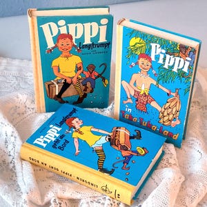May include: Three vintage children's books with colorful illustrations. The books feature the title "Pippi" in large white letters on a blue background. The illustrations depict a young girl with red braids and various scenes.
