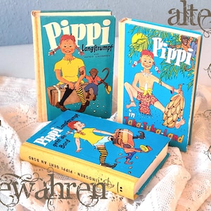 May include: Three vintage children's books with colorful illustrations of Pippi Longstocking. The books have blue covers with images of Pippi and text in German. The books are arranged on a white lace surface.